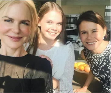 Three women smiling indoors, well-lit kitchen background, with a bowl of oranges in view.