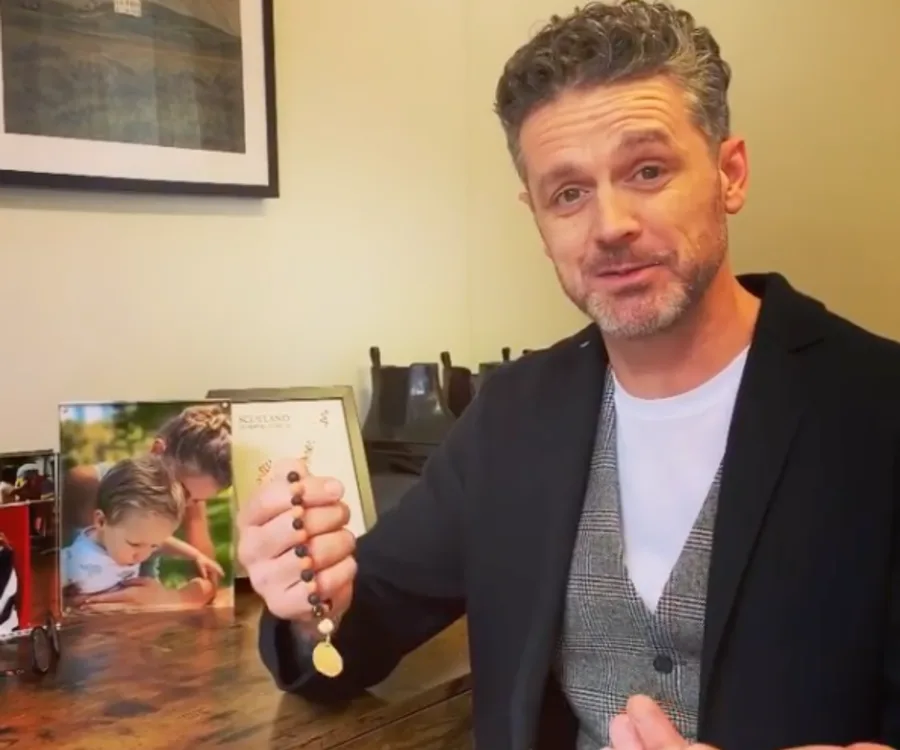 Man holding worry beads with framed photos on a desk behind him.