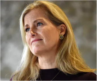 A woman with long blonde hair and decorative earrings, looking thoughtfully to the side against a blurred background.