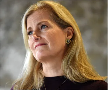 A woman with long blonde hair and decorative earrings, looking thoughtfully to the side against a blurred background.