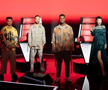Contestants and a coach pose on "The Voice 2020" stage with red chairs in the background.