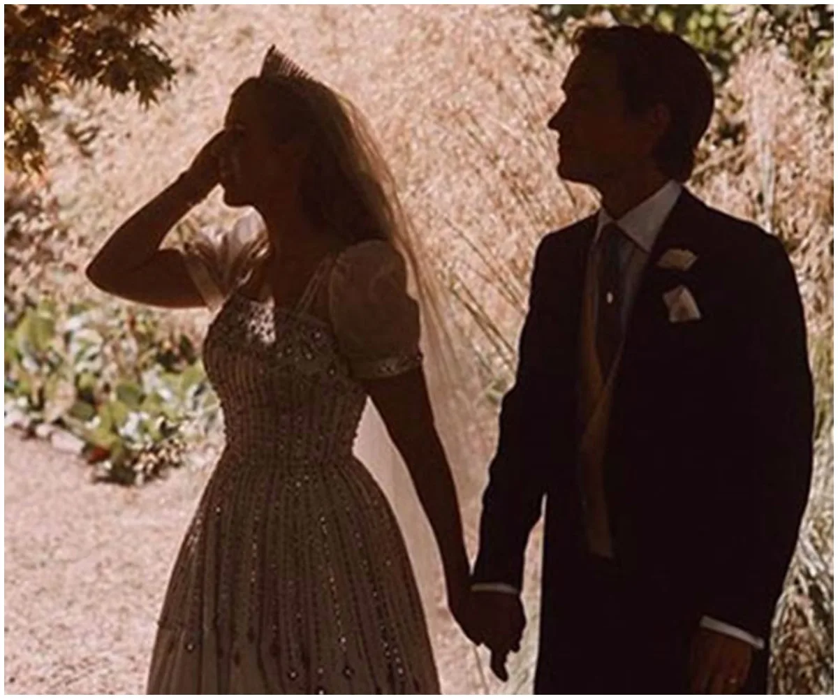 Silhouetted couple holding hands, bride in beaded gown with tiara, outdoors with light filtering through trees.