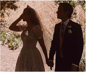 Silhouetted couple holding hands, bride in beaded gown with tiara, outdoors with light filtering through trees.