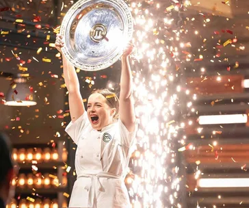 Chef celebrating victory on MasterChef stage, holding trophy with confetti and sparks in the background.