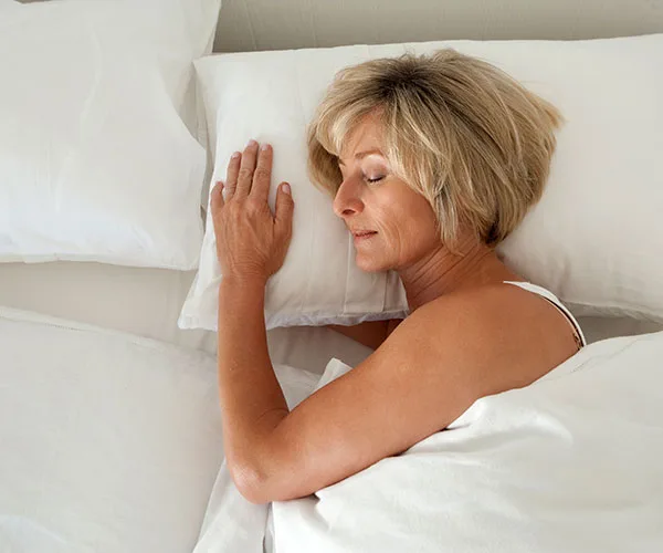 A woman peacefully sleeping on her side in a bed with white sheets and pillows.