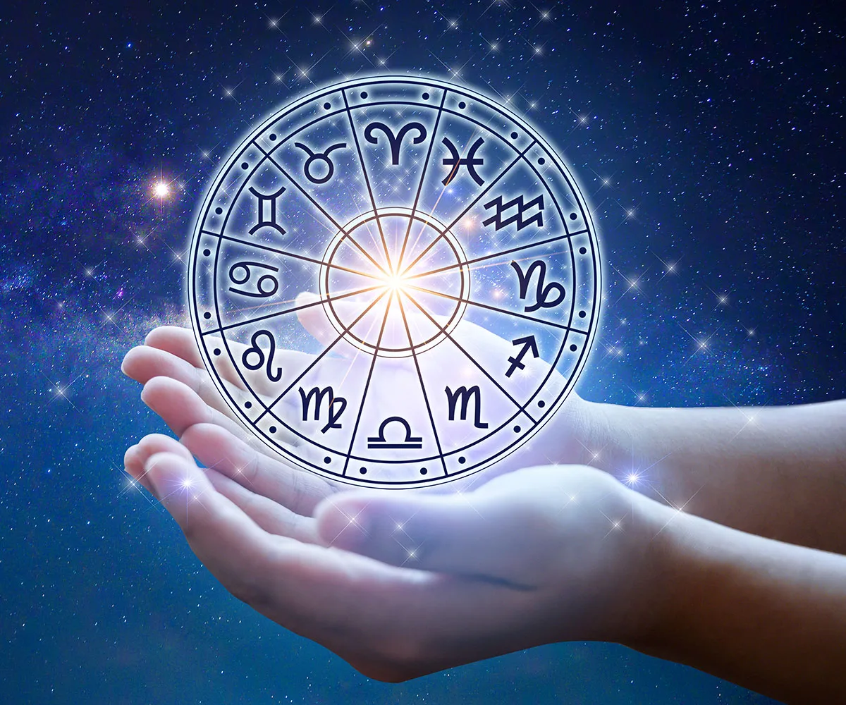 "Hands holding a glowing zodiac wheel against a starry night sky, depicting all twelve zodiac symbols."