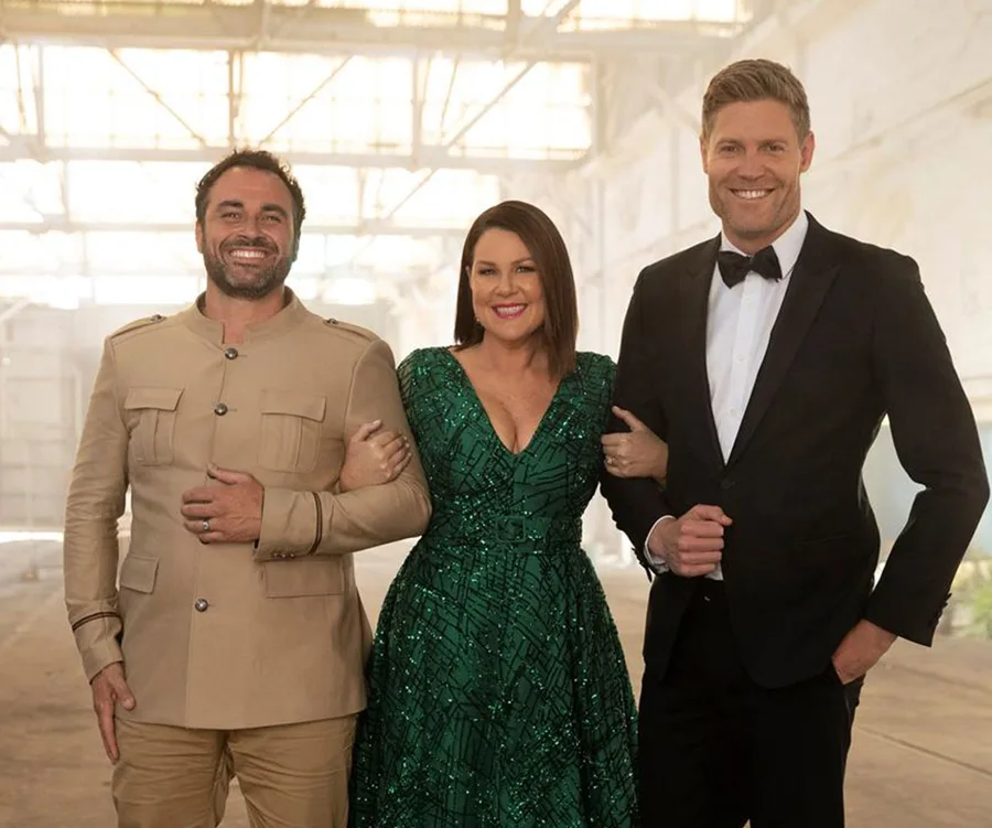 Three people smiling indoors; one in a tan outfit, another in a green dress, and the third in a black suit and bow tie.