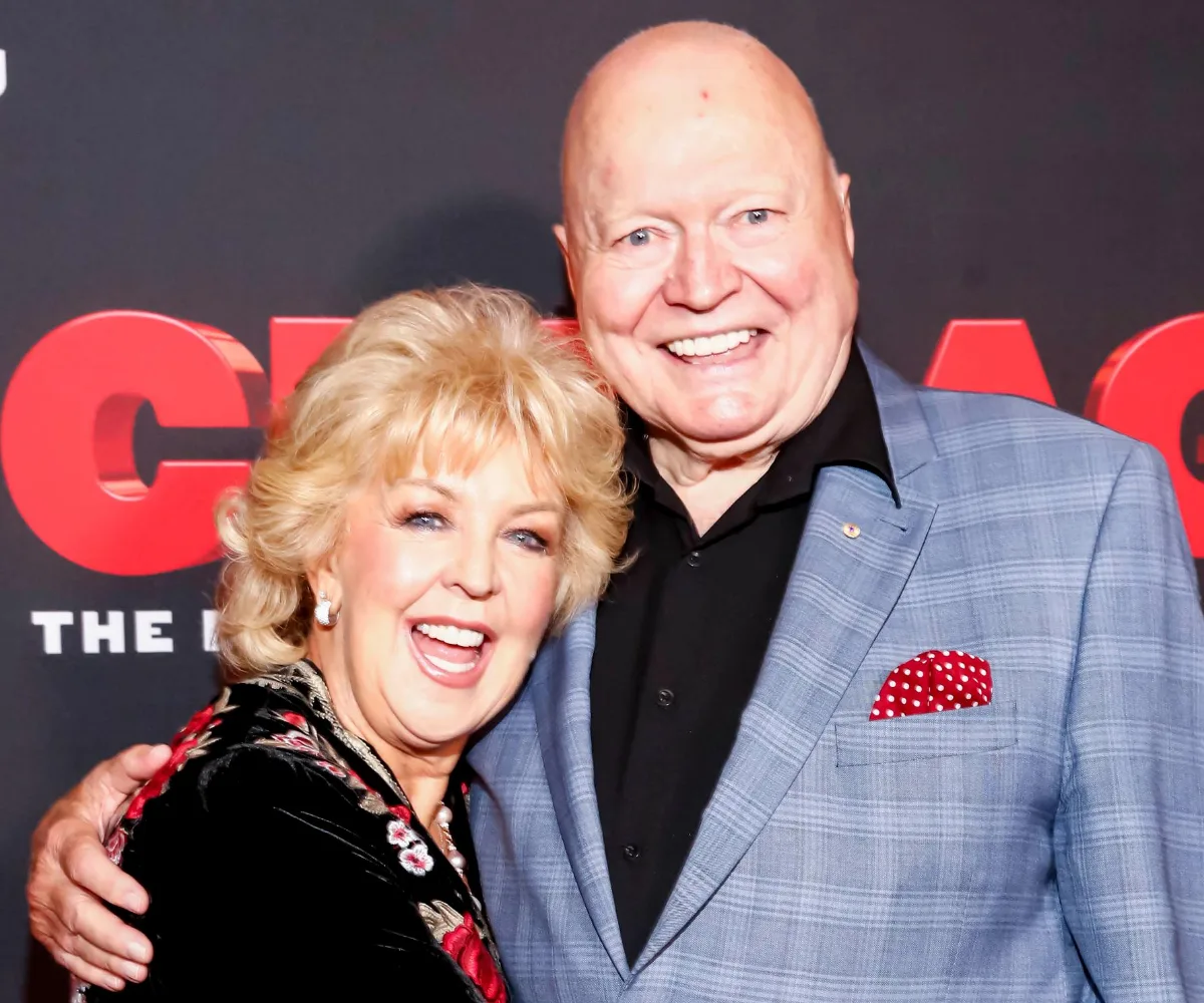 Two smiling individuals posing together at an event with a red and black backdrop.