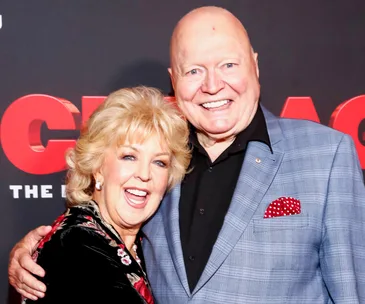 Two smiling individuals posing together at an event with a red and black backdrop.