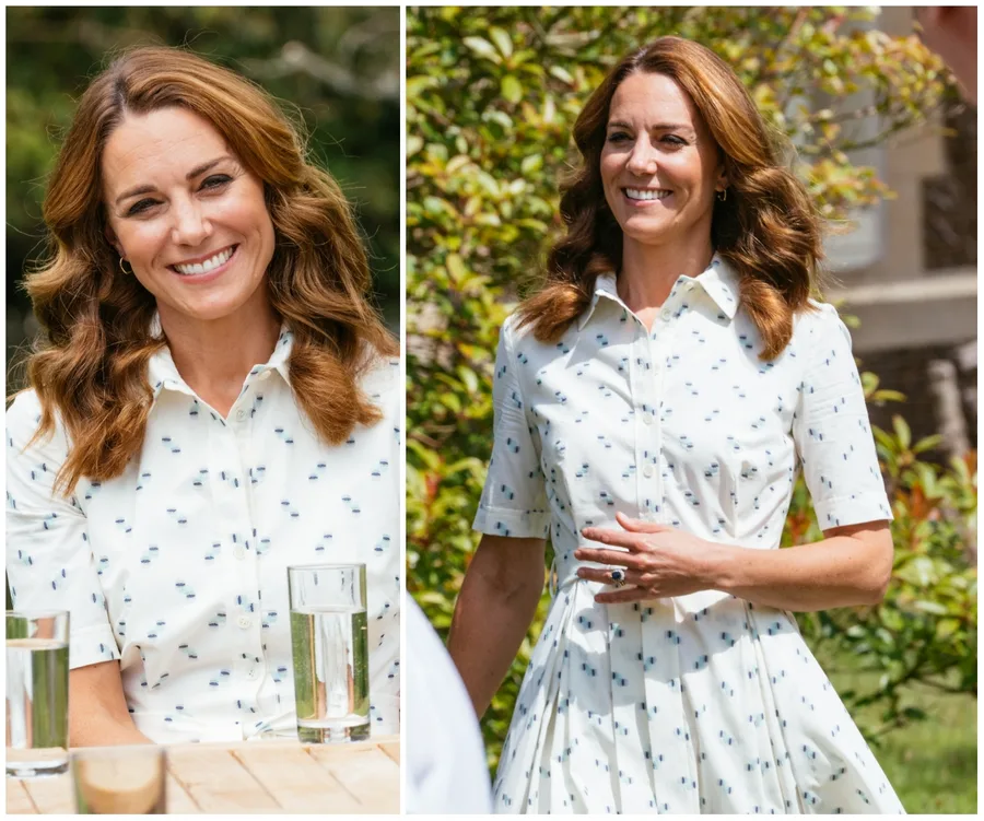 A woman in a white patterned dress smiles outdoors, with trees in the background, seated at a table with water glasses.