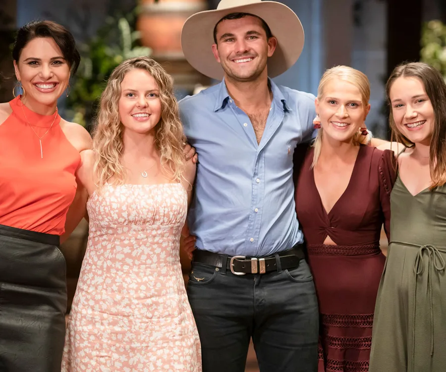 Group of five people smiling, including a man in a cowboy hat, posing together indoors.