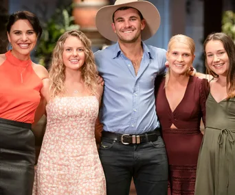Group of five people smiling, including a man in a cowboy hat, posing together indoors.