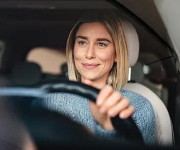 Woman smiling and driving a car, viewed from the passenger seat.