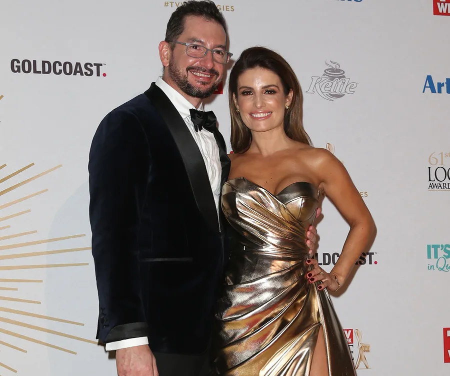 A couple posing at a formal event, the woman in a metallic dress and the man in a suit.
