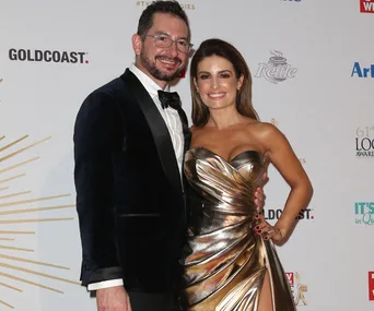 A couple posing at a formal event, the woman in a metallic dress and the man in a suit.