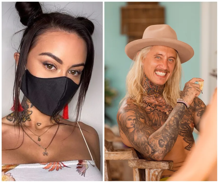 Two individuals; one with a mask and floral top, the other with a hat and tattoos, sitting and smiling.