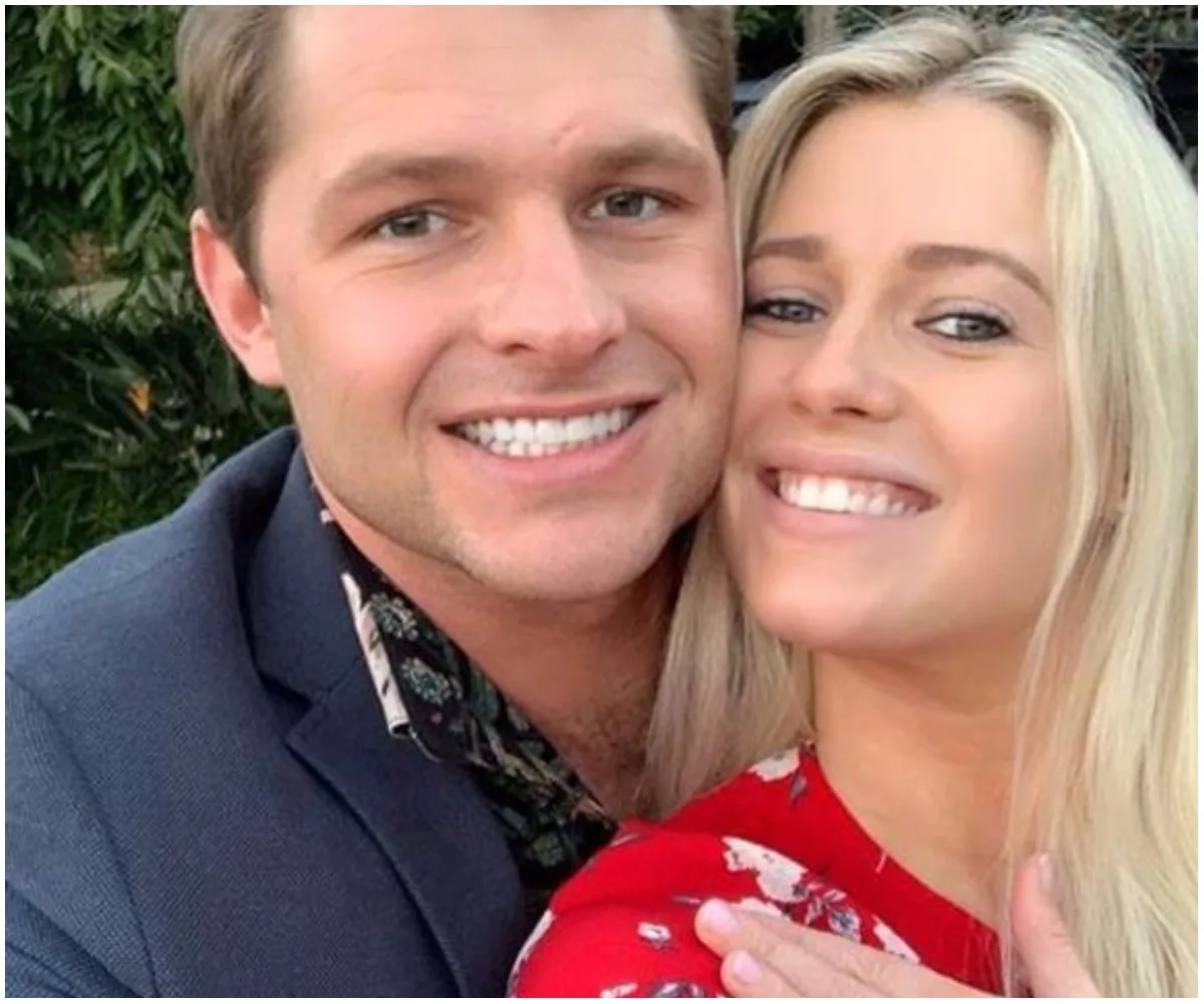 A couple smiling, with the woman showing an engagement ring, embraced and happy outdoors.