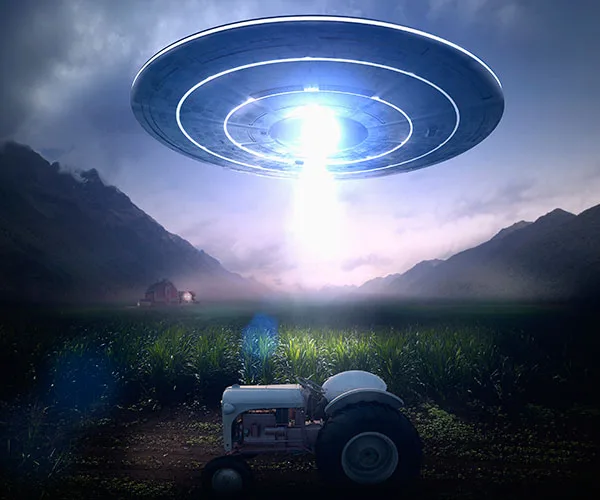 UFO hovering over farm field with beam of light, tractor in foreground, mountains and barn in the background.