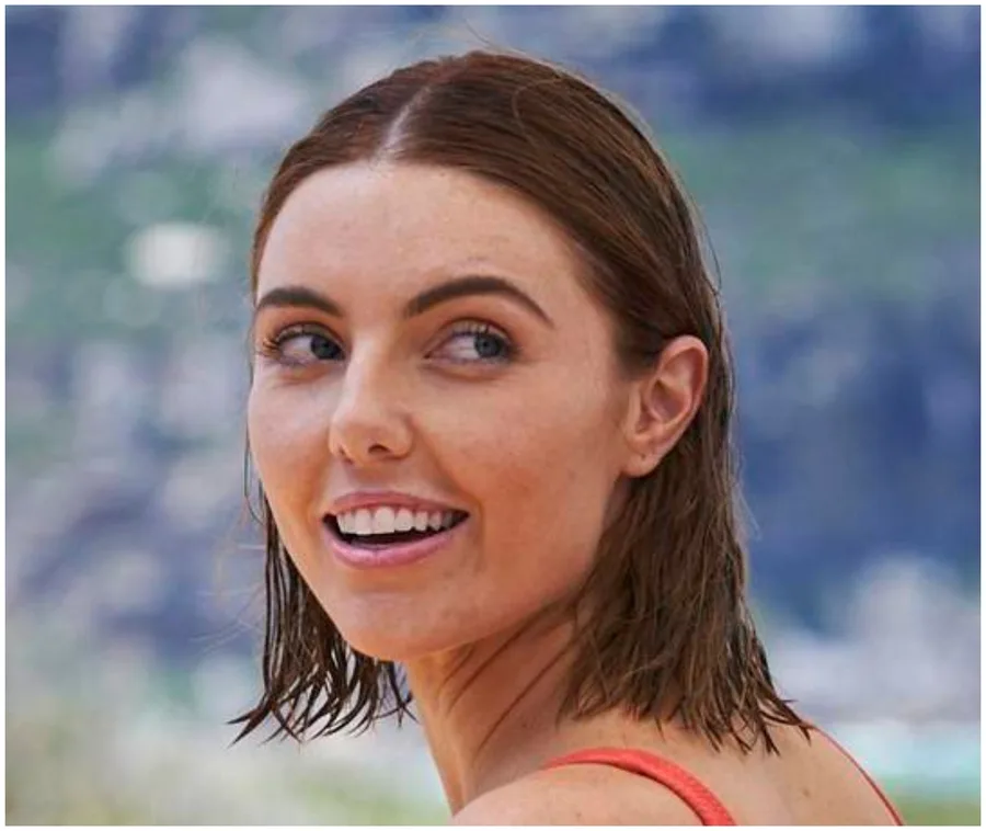 Smiling woman with wet hair looks back towards the camera, beach background slightly blurred.