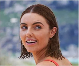 Smiling woman with wet hair looks back towards the camera, beach background slightly blurred.