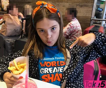 Girl in a "World's Greatest Shave" shirt pointing at it, holding fries, sitting indoors.