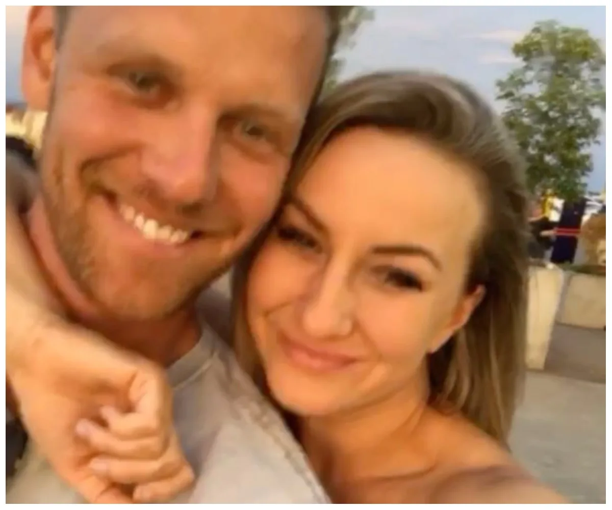 A smiling couple takes a close-up selfie outdoors with trees in the background.