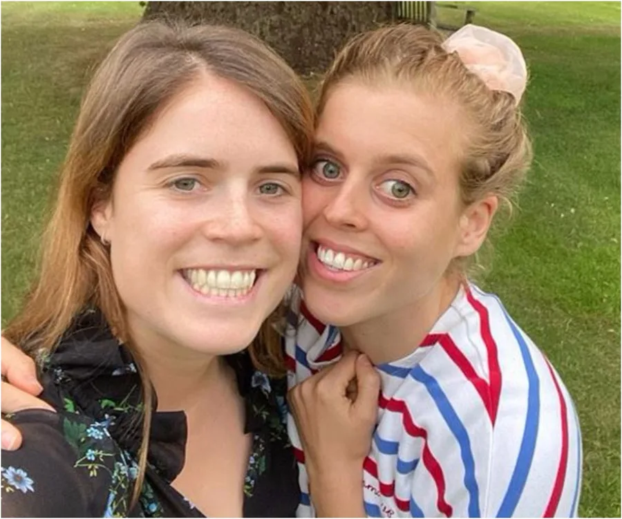 Two women smile in a selfie, standing close together outdoors, one in a striped shirt.