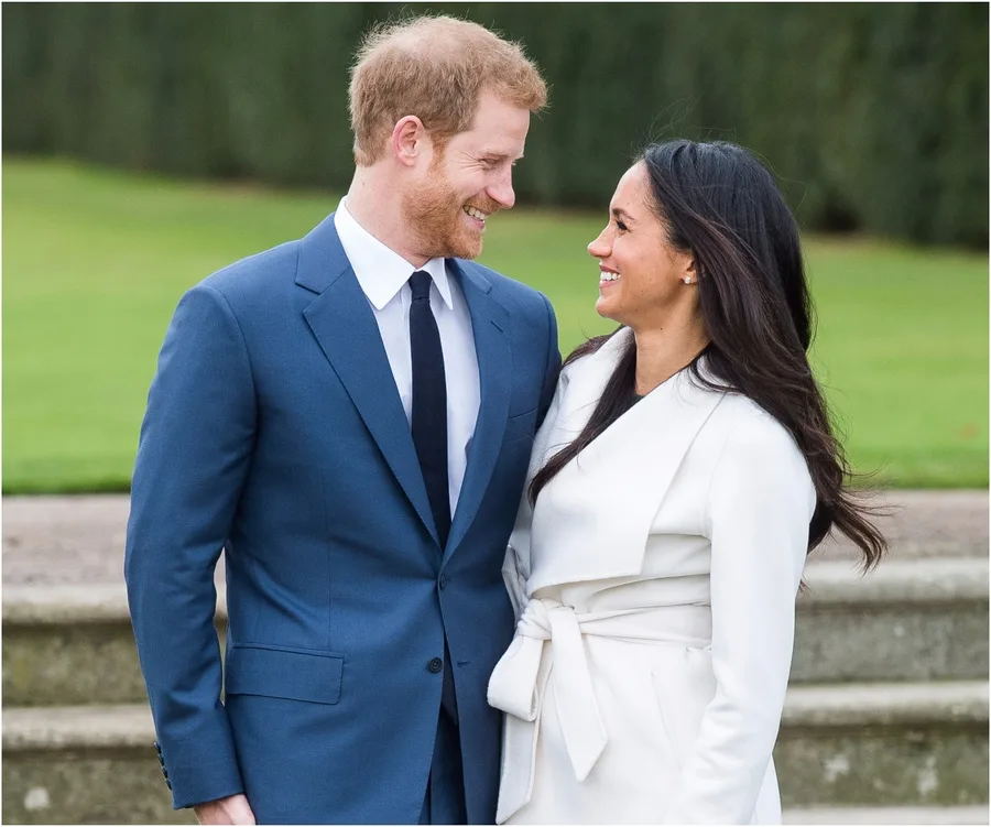 Prince Harry and Meghan Markle smiling at each other, outdoors, wearing formal attire.
