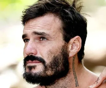 A man with short dark hair and a beard looks pensively into the distance.