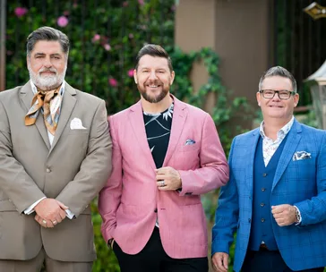 Three men in suits stand together outdoors, smiling at the camera.
