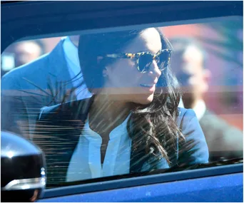 A woman with long hair and sunglasses, smiling from inside a car.