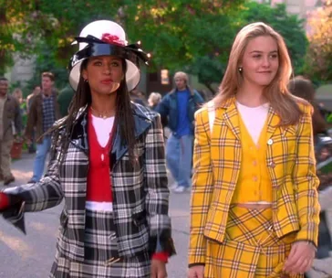Two women walking outside, one in a black plaid suit and hat, the other in a yellow plaid outfit, from "Clueless".