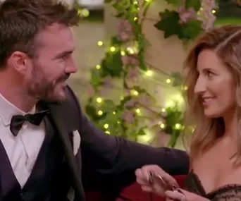 A couple smiling and sitting together, surrounded by soft lights and blooming flowers.