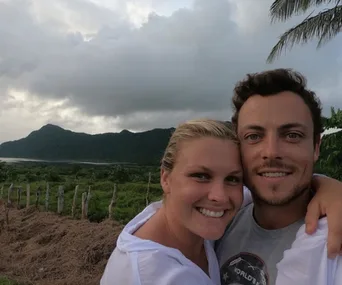 A couple smiling with mountains and cloudy sky in the background.