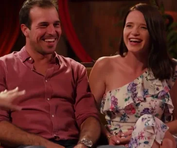 A couple laughing together while seated, with warm lighting and red curtains in the background.
