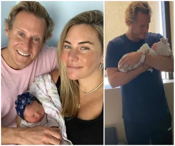 Man and woman smiling with a newborn baby in their arms, plus man holding baby, wearing a dark shirt.