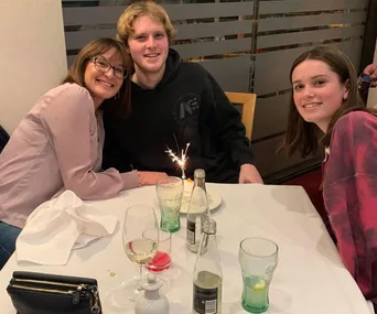 Smiling family gathered at a restaurant table with drinks and a lit sparkler on a birthday cake.