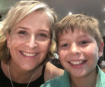 Mom and young boy smiling together in a close-up selfie indoors.