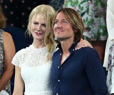 Couple smiling and embracing at an event, woman in white lace dress and man in navy shirt.