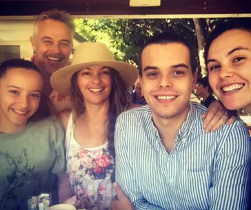 A group of five people smiling at the camera outdoors; one woman wearing a straw hat.