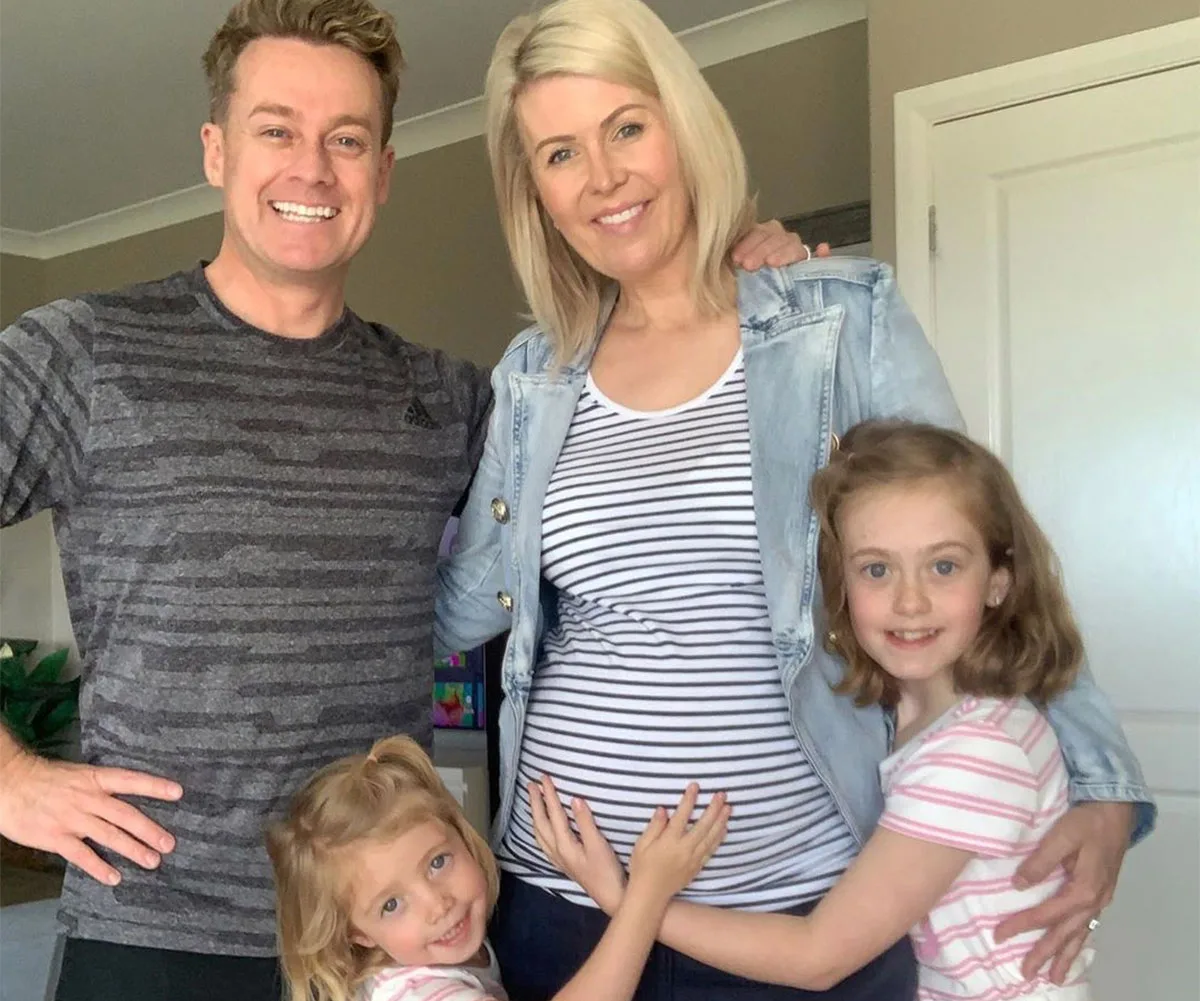 "Smiling family of four, two children touching mother's baby bump in a cozy home setting."