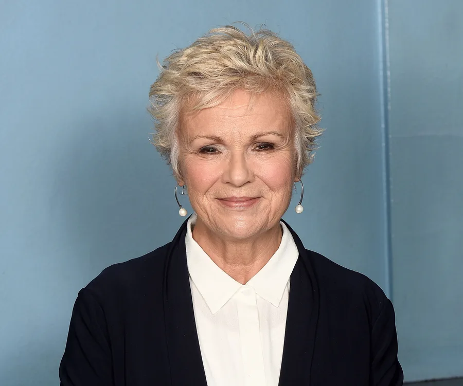 Julie Walters smiling, wearing a navy blazer and white shirt against a blue background.