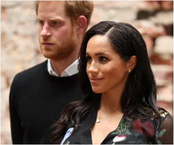A man in a black sweater and a woman in a floral dress in a brick setting.