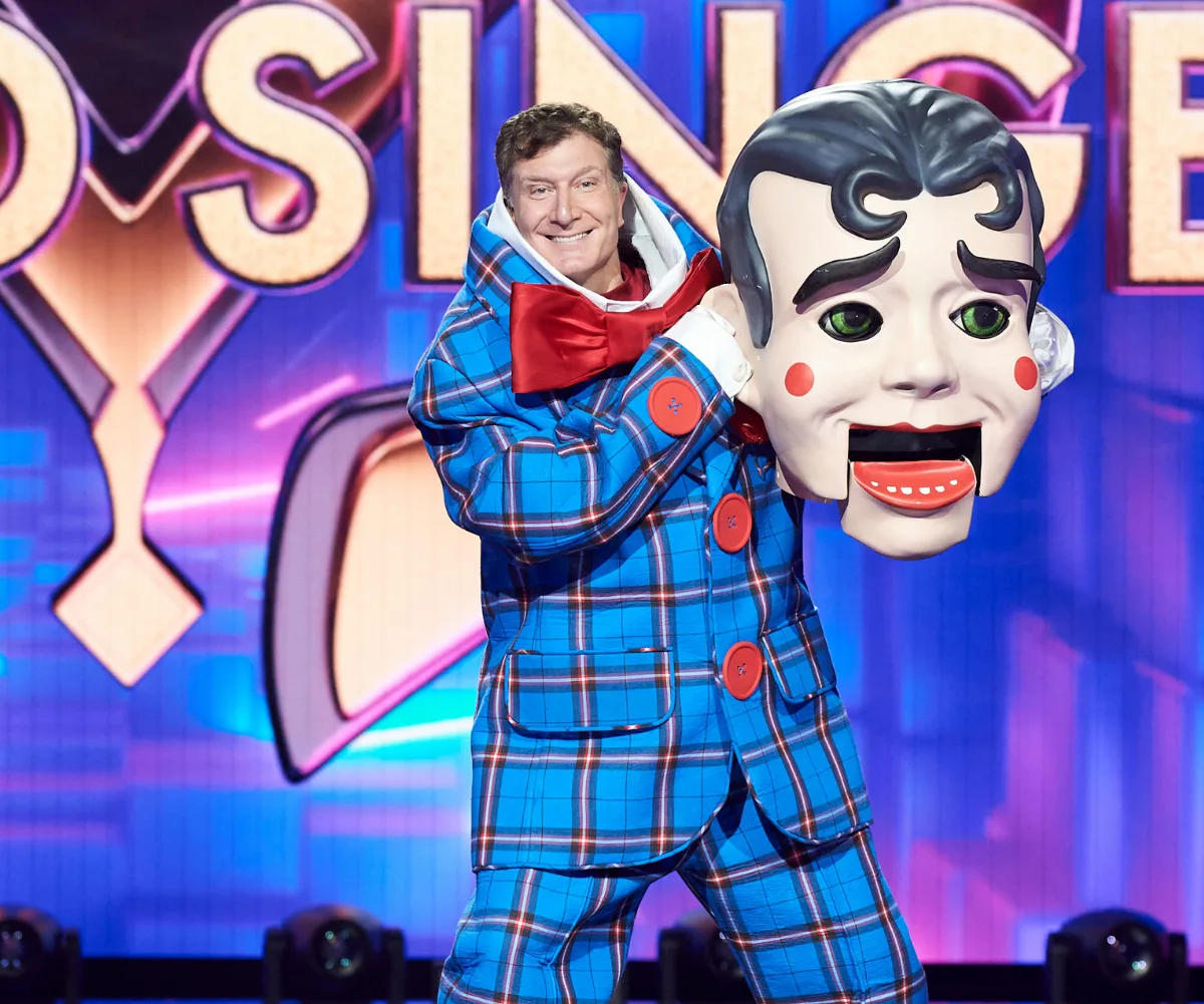 "Puppet character revealed on The Masked Singer Australia stage, performer holding large mask, vibrant colorful background."