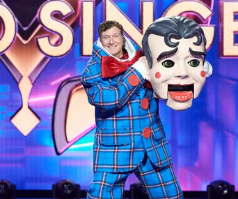 "Puppet character revealed on The Masked Singer Australia stage, performer holding large mask, vibrant colorful background."
