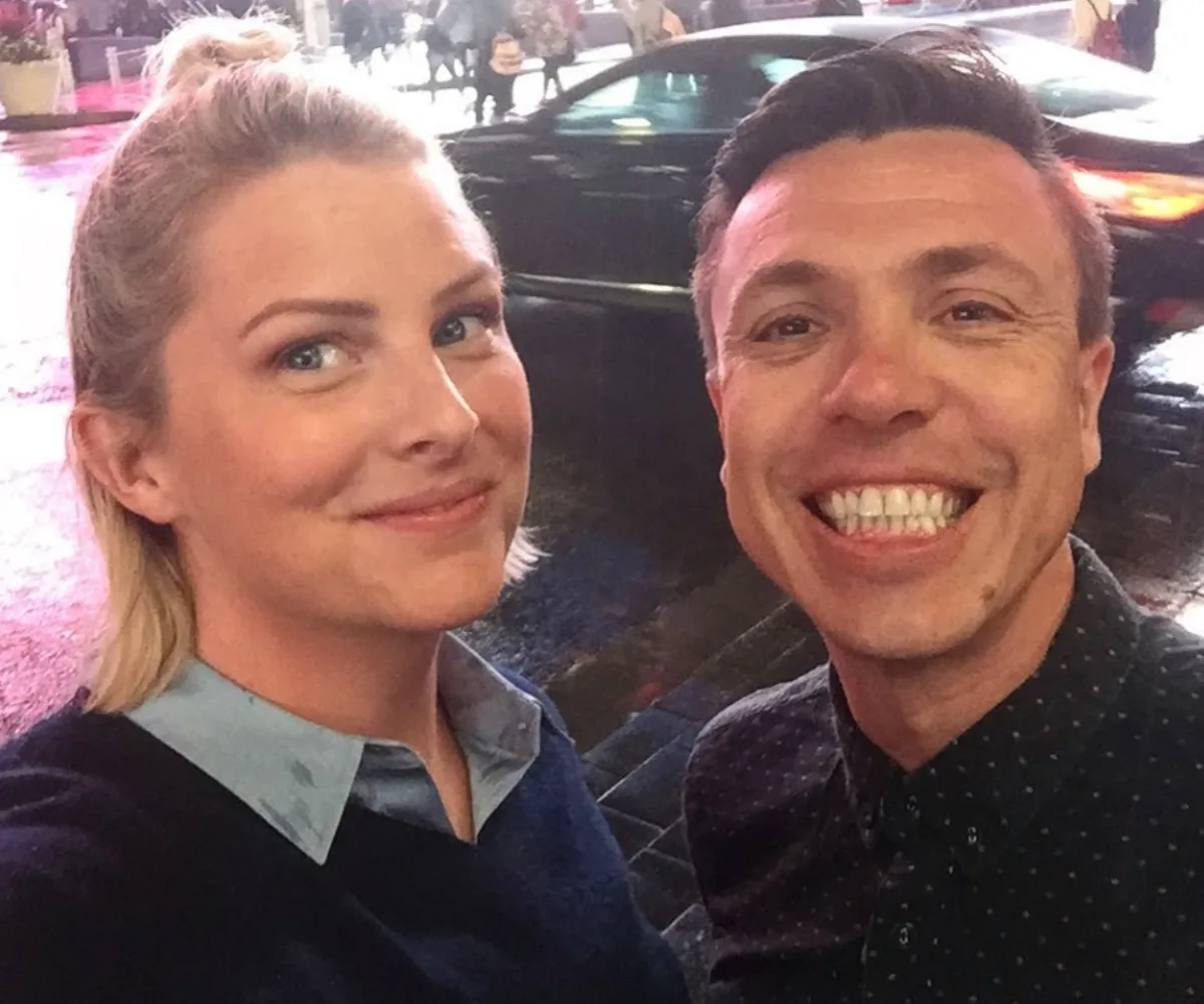 Two people smiling for a selfie on a rainy street with blurred car lights in the background.