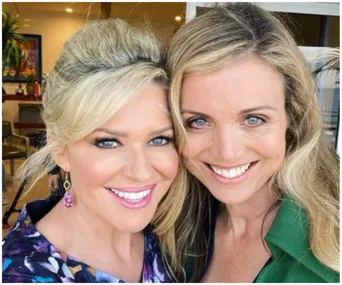 Two smiling women take a selfie together indoors with a warm ambiance.