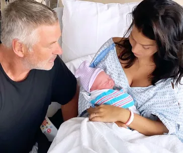 Man and woman in hospital holding newborn baby wrapped in striped blanket; woman in hospital gown.