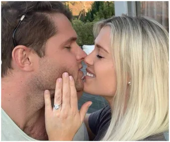 A couple sharing a tender moment, the woman displays an engagement ring, smiling with closed eyes.