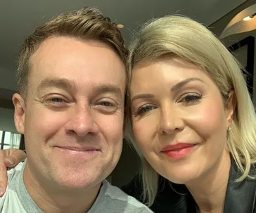 Selfie of a smiling couple in a bright room, both looking at the camera.